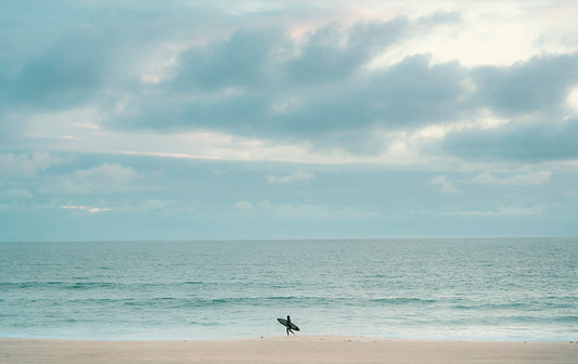 Photo of a single surfer walking along the shoreline in Manhattan Beach, CA.